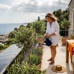 Woman tending plants on villa terrace with sea view