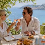 Couple enjoying drinks on sunny terrace by sea